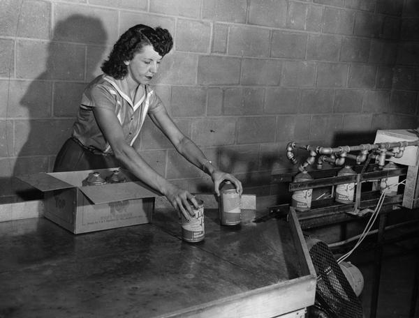 A woman production line worker boxes cone-top cans of Tip Top soft drinks as they come off the production line.