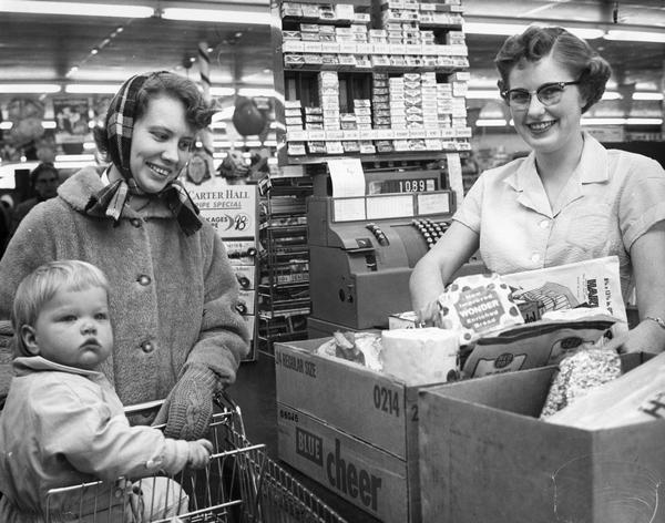 A grocery clerk boxes up purchases as a woman and her young son wait at the checkout counter.