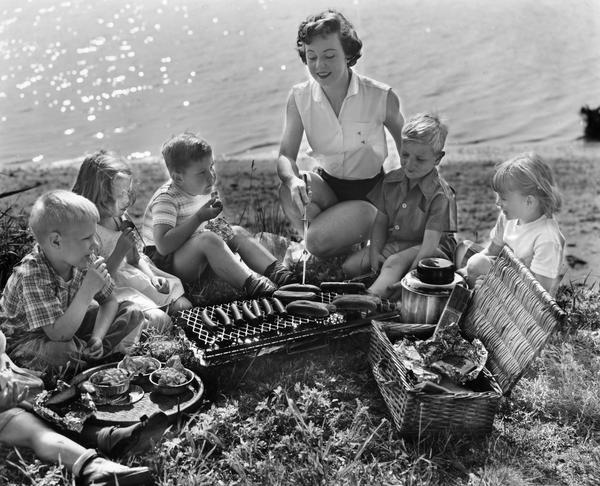 Woman with children grilling hot dogs and wieners at the beach.
