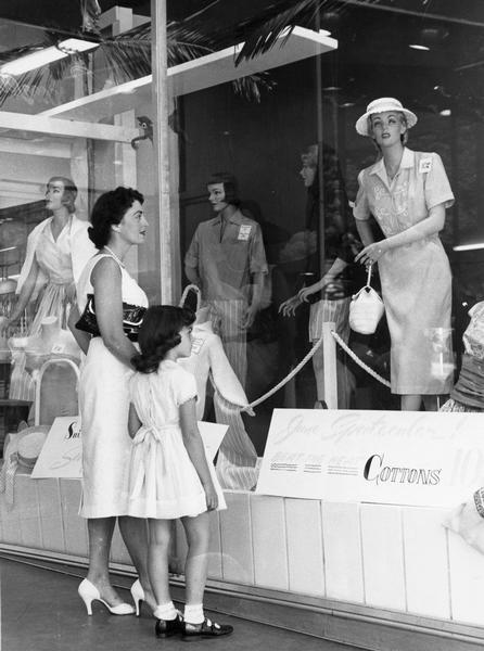 A woman and young girl review the latest fashion merchandise in a retail window display.