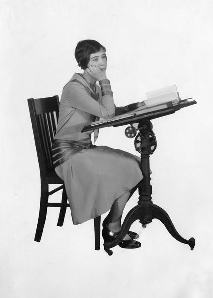 Adolescent schoolgirl Miss Genivieve Graves seems to be daydreaming at her school desk.