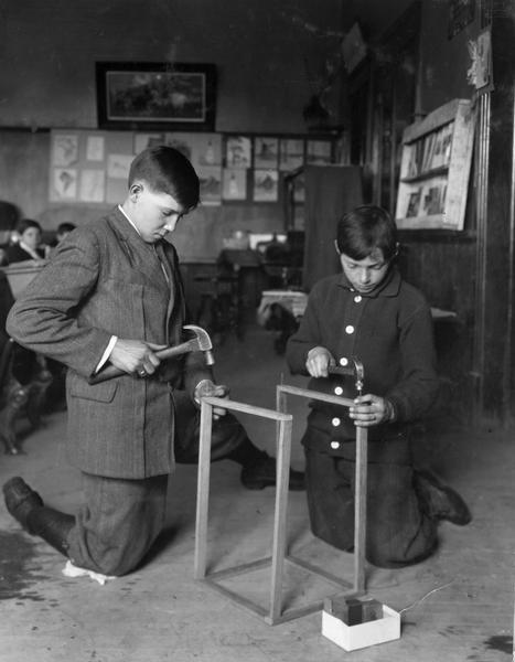 Two boys at work indoors constructing the wooden frame of a fly trap at their school.