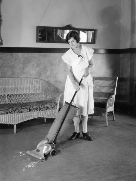 Woman vacuuming rug with a "Vacuette" sweeper in a farmhouse living room.