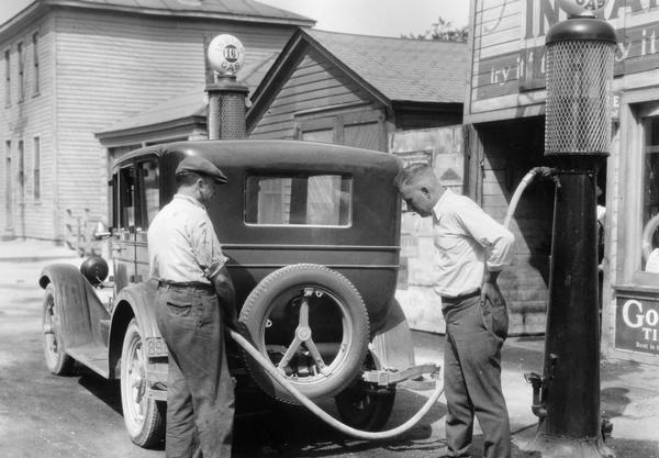 Men filling the gas tank of an automobile at an "Indian Gas" roadside service station. The photograph was taken for International Harvester's Agricultural Extension Department. It was used to warn families of potential farm hazards. The original caption reads: "Don't shake or allow motor to run while filling gasoline tank."