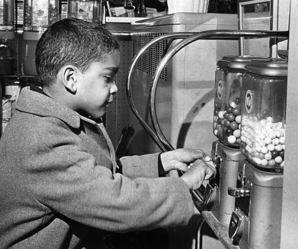 Boy inserting coin into a gumball vending machine in anticipation of a sweet treat.