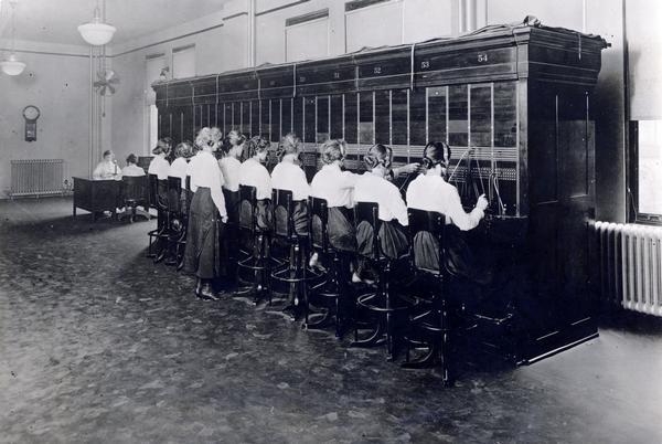 Women work on nine-place telephone switchboard that served 1,145 single-line flat-rate telephones originating 10 calls per day, on average.