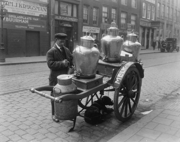 A milkman pauses to dispense milk from the tap of a large milk can on his dog-powered delivery cart in Rotterdam, Holland.