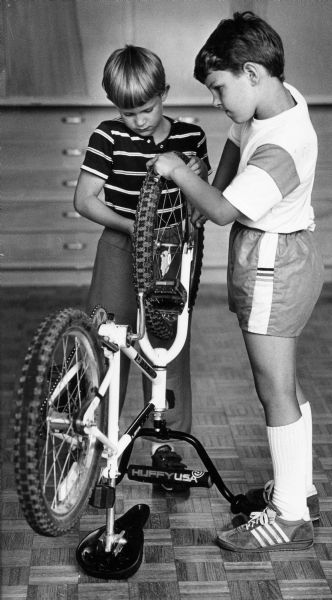 One boy steadies a bike while his friend tightens the nut on the front wheel to complete a tire repair.