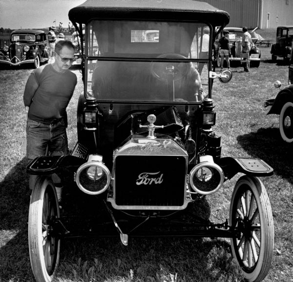 At a Hartford antique show, a man looks over a well-maintained Model T Ford. In the background other people inspect more vintage automobiles.