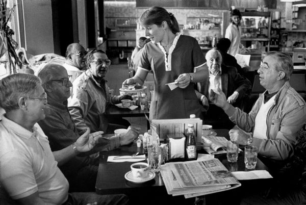 A waitress serves a group of older Italian-American men in a diner.