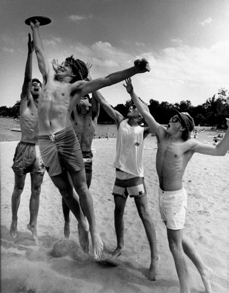 Young men clamor to catch a Frisbee during a beach game.