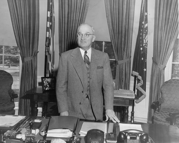 Harry S. Truman in the oval office standing behind his desk.