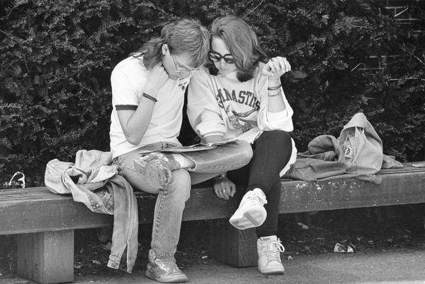 A couple holds hands and reads together while sitting on a bench.