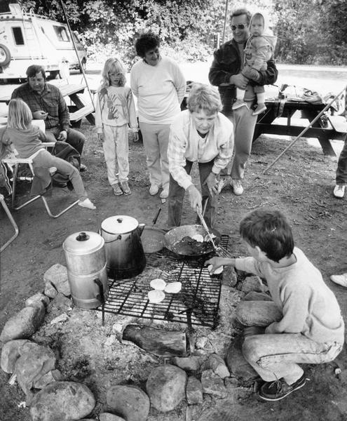 Family members gather around a campfire to enjoy biscuits and sausages cooked on the grill at Naga-Waukee Park.