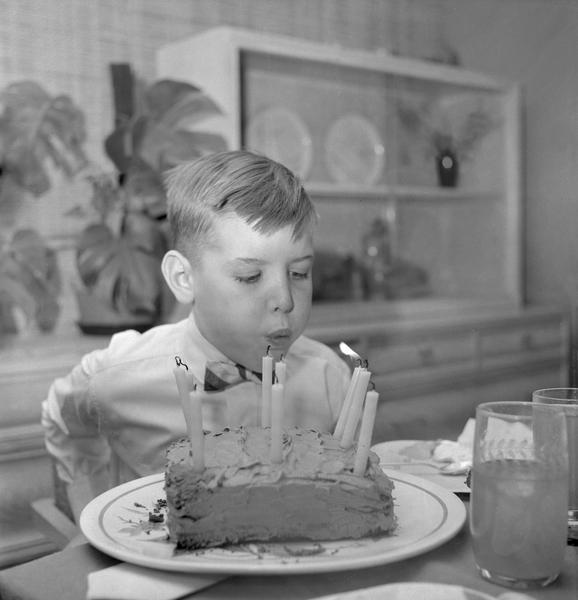 A boy blowing out 9 candles on a birthday cake.