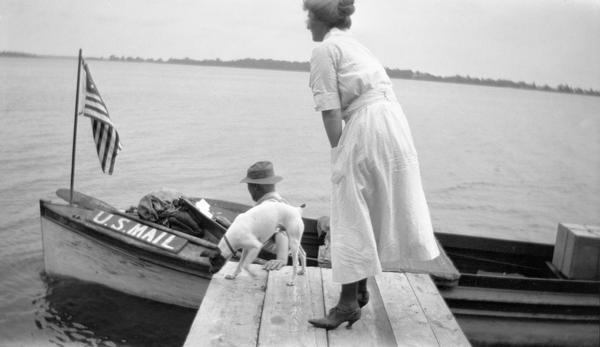 A woman and her dog meet the mail carrier in his delivery boat at the end of a pier on the west shore of Fox Lake.