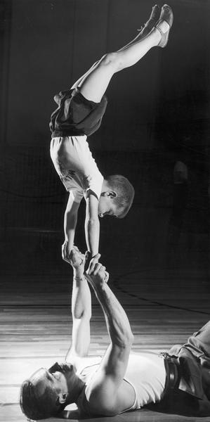 A man laying on the floor provides the base for a boy to perform a handstand.