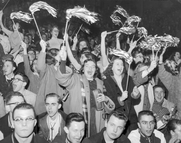 High school fans in the bleachers cheer on their team during a night game.