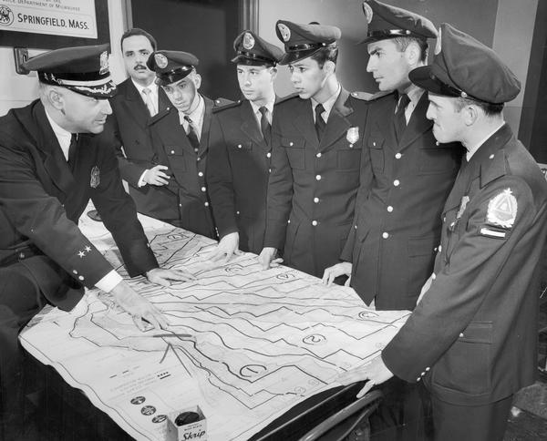 Uniformed police officers looking over a laid out map with potential escape routes.