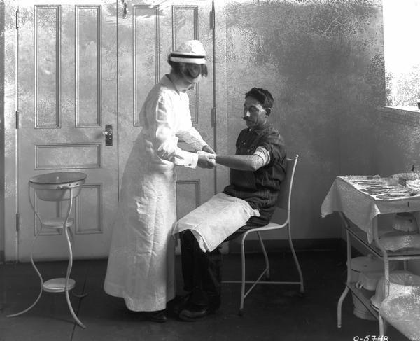 View of a nurse applying a bandage to the arm of a worker at an International Harvester factory (possibly Osborne Works in Auburn, NY).