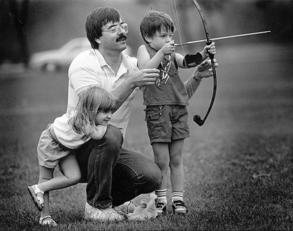 A father gives his young son archery pointers in Kletzsch Park while his daughter looks on.