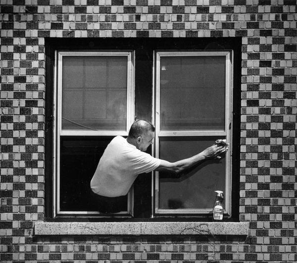 A man leans out a window to clean the outside glass.