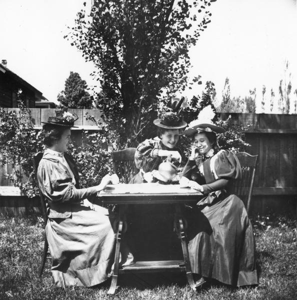 A woman pours tea for her friends seated outdoors at a table.