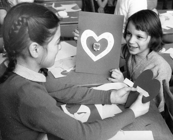Schoolgirls showing one another the valentines they are making in class to celebrate the holiday.