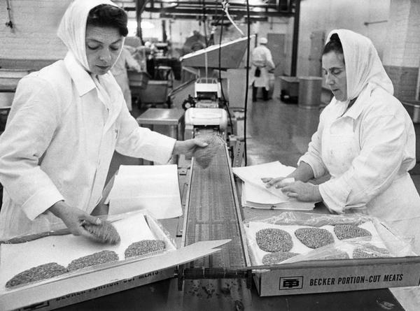 Workers are filling orders of ground steak patties by putting them into corrugated boxes layered with parchment divider paper.