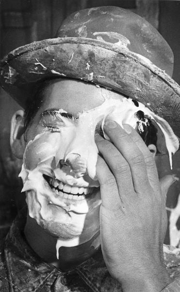 Roland Sieg wiping pie from his face while smiling, after someone threw enough ping pong balls in a bucket to win a chance to hit him with a pie at a carnival at the University of Wisconsin-Milwaukee.