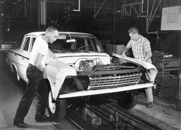 Auto workers attach fenders to a new car in the factory.