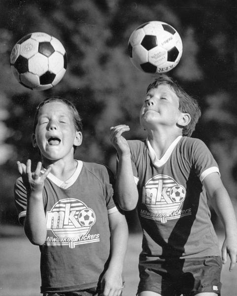 Twins from the Sting of Wauwatosa warm up for Milwaukee Kickers League soccer tournament. They are wearing matching t-shirts and are spiking two soccer balls with their heads.