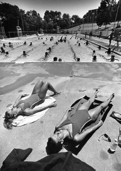 Two women lifeguards sun themselves at the edge of Horeb Park pool during a rotation break.