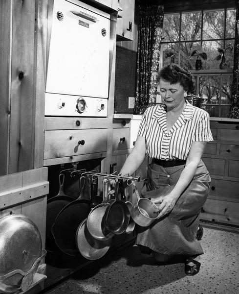 A woman shows how her variety of pots and pans are stored on a sliding rack under the oven in her kitchen.