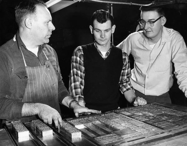 Sports editor and sports reporter from the "Wisconsin State Journal" confer with a printer over trays of lead type.