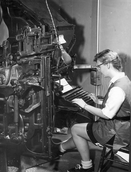 A woman types text into a linotype machine.