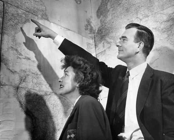 A man and woman look at wall-size maps as he points to the east coast of the United States.