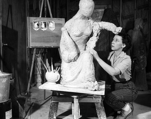 A female artist sculpting a female figure from clay.