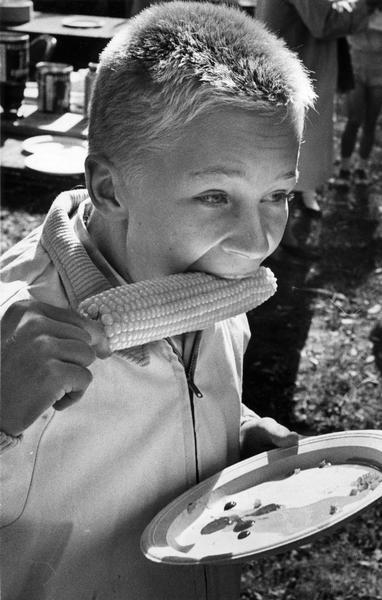 A boy eating buttered corn on the cob at a Golden Spike Day party.