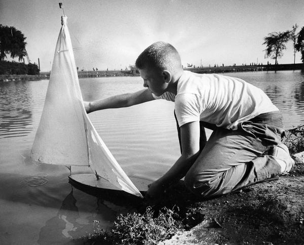 A young man launches his toy sailboat in the lagoon.