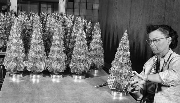 A woman fashions a miniature hand-made metallic tree, while tables full of others await packing and shipment for the Christmas holidays.