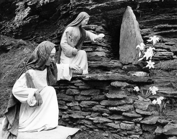 As part of an Easter tableau, a statue of Mary Magdalene at the entrance to what is a depiction of Jesus' tomb, is mirrored by a young girl in similar garb, kneeling nearby. This is one of several stations created at Biblical Gardens.