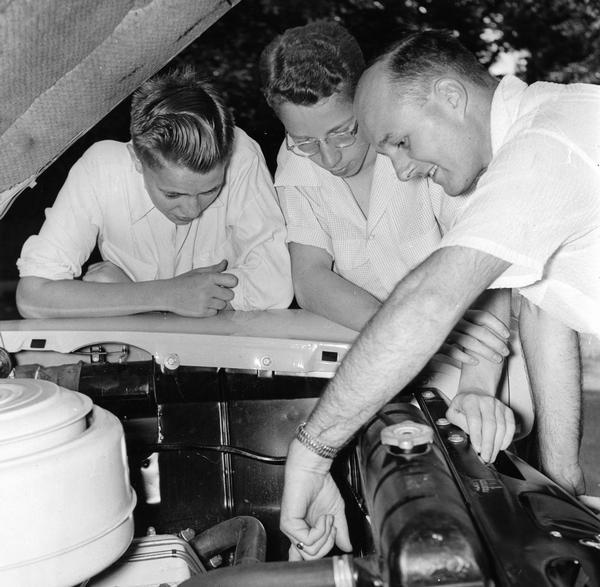 A man shows two teenagers the intricacies of what is under the hood of the family car.