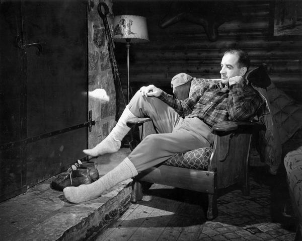 A vigorous campaigner, Joseph R. McCarthy relaxes in front of a log cabin fireplace after his electoral campaign.