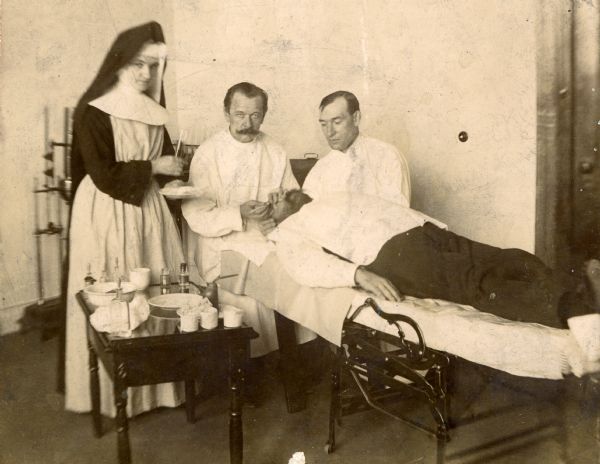 Dr. Joseph Schneider performs surgery on the eye of a man laying on a gurney, with assistance from a nun nurse and another man.