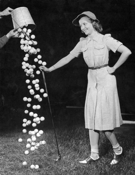 A woman dressed to play golf smiles as a bucket of golf balls is spilled at her feet.  This is one of several demonstrations of strobe light functions at Frank Scherschel's Strobo Research Lab.