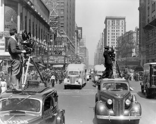 Parade of two International "Jungle Yachts" on Times Square, with newsreel cameramen on top of cars in front of the procession. The "Jungle Yachts" were specially produced by International Harvester for one of Commander Attilio Gatti's expeditions to the African Congo.