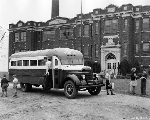 Students standing around an International D-30 school bus in front of Jefferson Township School. The bus is equipped with a nineteen-foot Hicks body.