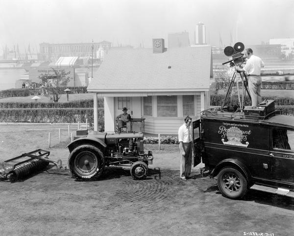 Cameraman and sound operator from Paramount Sound News on top of a truck filming a demonstration of the McCormick-Deering O-12 radio-controlled tractor and soil pulverizer at the "A Century of Progress" Worlds Fair. In the background across Burnham Harbor is Soldier Field and the Sears Roebuck and Co. building.