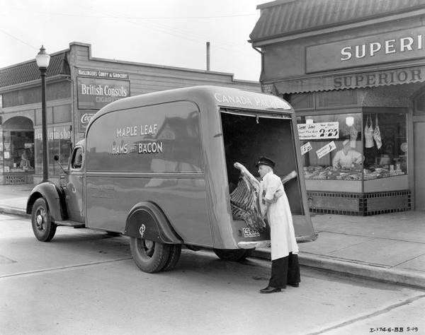 Man unloading a side of beef from a "Maple Leaf Hams and Bacon" truck outside a butcher shop in Vancouver, British Columbia, Canada. The truck is an International D-30 owned by Canada Packers.